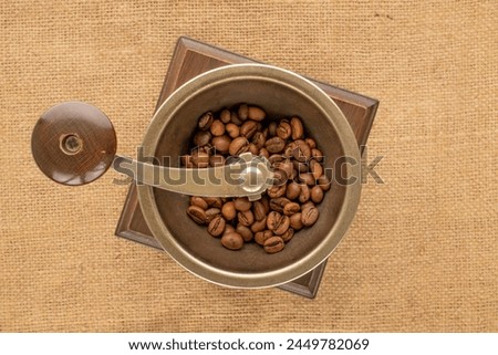 One manual, wooden coffee grinder with coffee beans on a jute cloth, macro, top view. Royalty-Free Stock Photo #2449782069