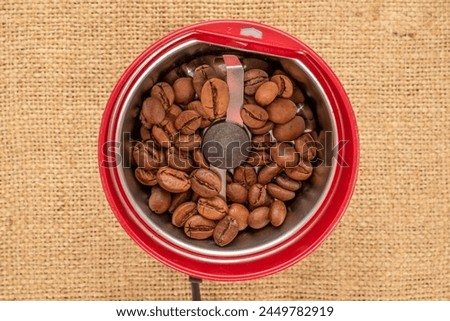 One electric coffee grinder with coffee beans on a jute cloth, macro, top view. Royalty-Free Stock Photo #2449782919