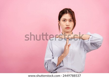 Young asian woman wearing long sleeve shirt and disappointed face while using both hands to showing time out gesture isolated over pink background.