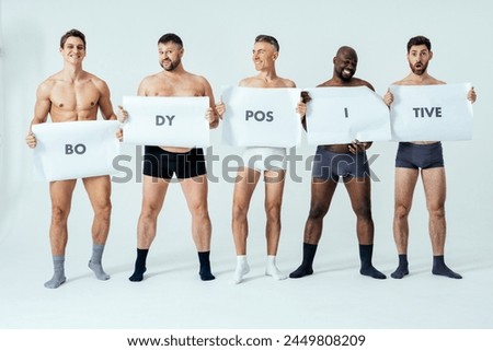 Multiethnic men posing for a male edition body positive beauty set showing messages on banners. Shirtless guys with different age, and body wearing boxers underwear.