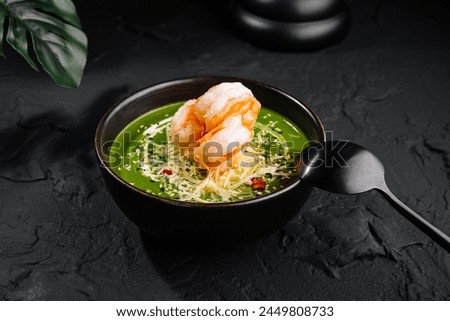 Gourmet presentation of shrimp spinach soup adorned with toppings in a dark bowl on a textured surface