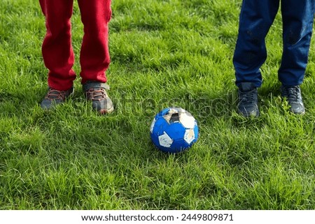  The legs of two boys in torn sneakers on the background of a torn  old soccer ball, EURO, FIFA World Cup, Summer Olympics, Paris 2024 Royalty-Free Stock Photo #2449809871