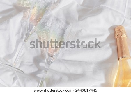 Romance concept, lifestyle photo minimal style, two bright glasses with rainbow shadow, white wine bottle on white bedclothes at home, natural light, top view close up, star filter effect, copyspace