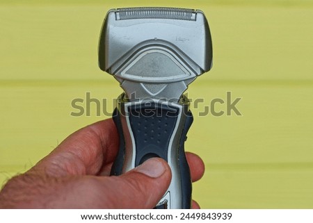 one electric gray plastic battery-powered modern men's razor with iron sharp blades industrial razor in hand on a yellow background