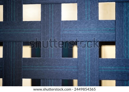 Wide strips of thick blue fabric are intertwined with each other. Grid background of blue lines. Sturdy fabric base for mattress close-up blue color