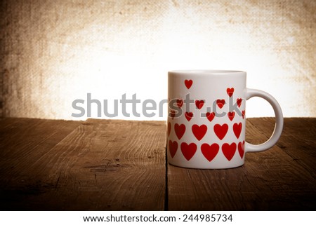 Mug with many pictured hearts on the old wooden table. Toned.