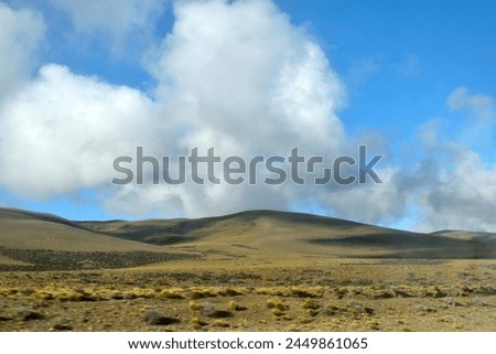 Photography of a placid and calm landscape, a field, slopes, hills and a sky with fluffy clouds