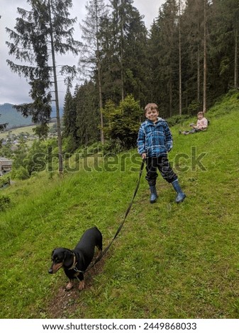 A boy with a dachshund dog and a girl are walking in the forest against the background of mountain peaks and roofs of village houses, active family vacation, twins. Photo.