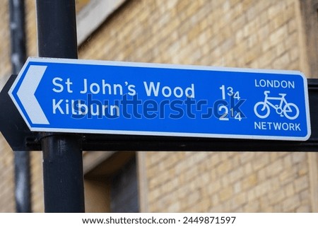 Close-up of a direction sign for cyclists showing the direction and mileage to St. John's Wood and Kilburn in London, UK.