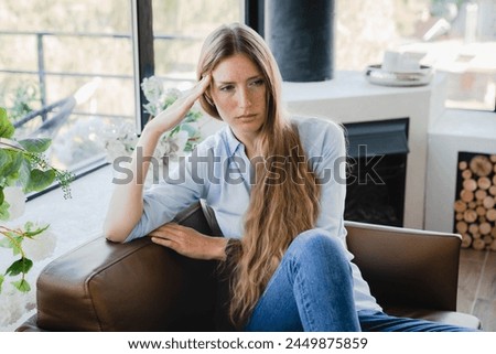 Pensive young woman sitting in the armchair thinking about sad problems issues at home. Depressed female lady girl having period crumps, nostalgy, relationship breakup Royalty-Free Stock Photo #2449875859