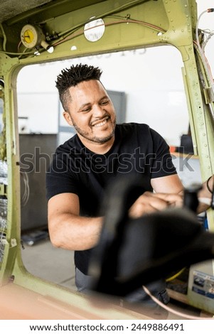 Vertical photo of a dark-skinned man in uniform fixing a broken plane. The Latino engineer is fixing the aircraft's controls. Concept of Dominican technicians or engineers.