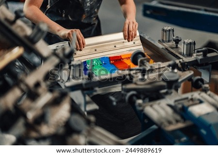 Close up of female experienced graphic technician's hands silkscreen printing with squeegee at printing workshop.Cropped picture of unrecognizable print shop worker suing rubber blade for screen print