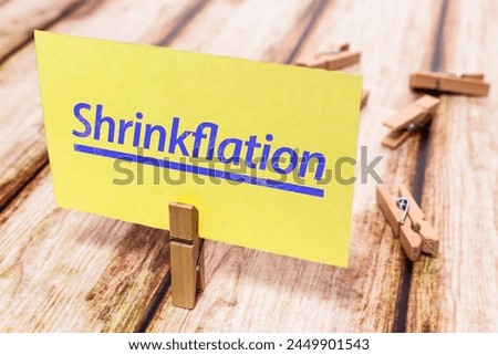 Conceptual message card showing Shrinkflation on shabby wooden table. Nice wooden clothespin or natural wooden pinch holding yellow paper note. Royalty-Free Stock Photo #2449901543