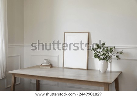 Breakfast, scandi interior still life. Minimal home design. White ceramic vase with blooming apple tree branches. Cup of coffee, tea on wooden table, desk with old books, blank picture frame mockup.