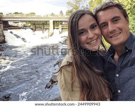 A cute couple takes a selfie in front of a waterfall and Rapid Dam Royalty-Free Stock Photo #2449909943