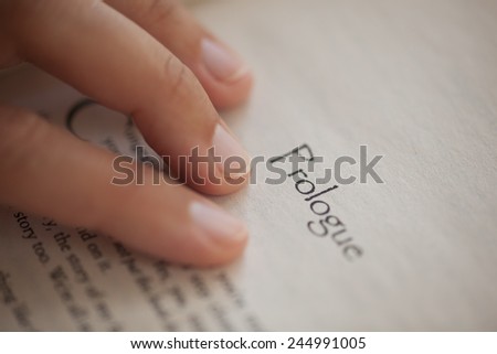 Woman's hand on book page with title "Prologue". Shallow depth of field. Royalty-Free Stock Photo #244991005