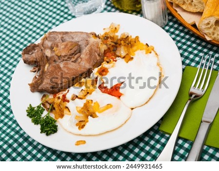 Picture of delicious fried pork with fried eggs at plate on table
