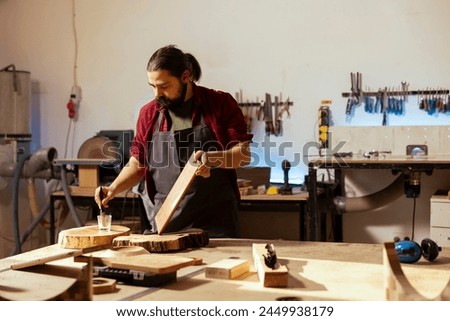 Cabinetmaker applying varnish on wooden surface to prevent damage and provide layer of protection. Woodworking specialist in carpentry shop doing finishing on wood plank, putting coats of oil Royalty-Free Stock Photo #2449938179