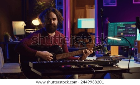 Musician plays acoustic guitar and records melody to compose new song and tunes. Computer screen showing DAW software interface with soundtracks, sound engineer in music production. Camera A.