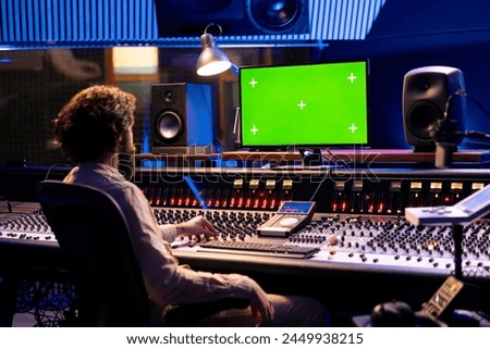 Sound designer working on mixing and mastering tracks with mockup display, using control panel board in professional studio. Skilled producer looks at greenscreen, editing music.