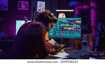 Audio technician mixing and mastering songs on daw software, creating fun atmosphere with acoustics and amplifier. Sound designer recording tunes on dj panel board in his home studio. Camera B.