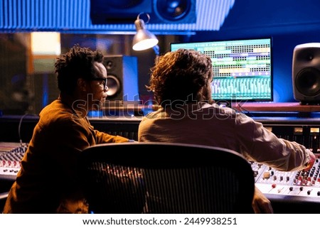 Team of technical engineers working on recording and editing music in professional studio, collaborating on mix and master audio files to create a new hit song. Artist and expert in control room.