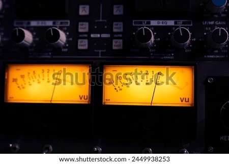 Technical recording equipment and devices for calibrating volume levels and sound settings in professional studio control room, yellow light. Audio mixer desk with switchers and sliders. Close up.