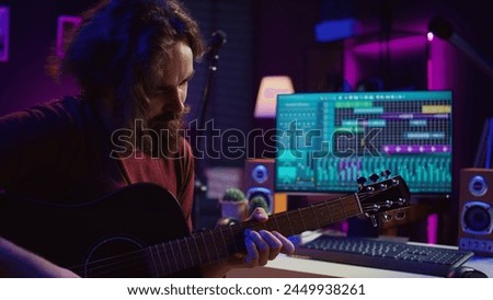 Young man playing guitar and creating music using equalizer daw software interface. Music producer recording song in home studio and mixing acoustic sounds on stereo console. Camera B.