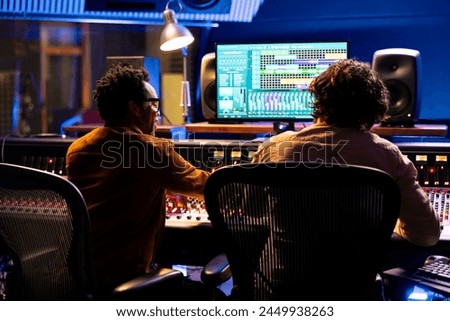 Professional sound engineer and artist working together on a new track, using digital audio software to edit and process tunes. Experts team collaborating on music, mixing at control room board.