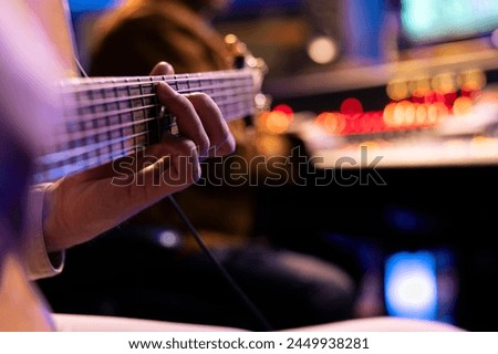 Talented singer playing new accords on electro acoustic guitar in music studio, recording new songs with audio engineer in control room. Male musician producing tracks on instrument. Close up.