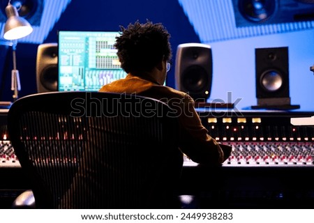 African american record engineer editing and mixing songs on studio console, using digital software on monitor to add audio effects in post production. Producer working on new music.