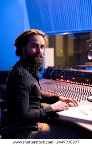 Portrait of sound engineer working with audio console and digital software on pc in professional recording studio, producing tracks for an album. Technician editing new songs in control room.