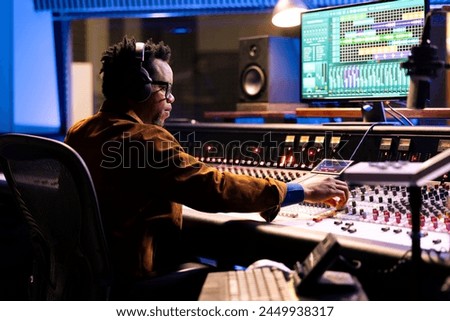 African american sound producer uses compressor and mixer in professional recording studio, adjusting volume levels and audio settings on a track. Music production concept in control room.