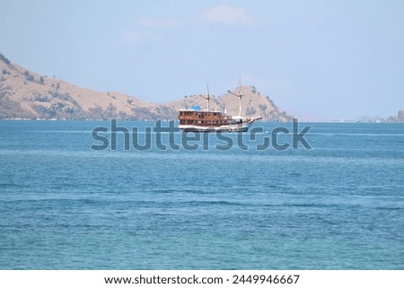 a traditional wooden boat called phinisi is in the middle of the blue sea in the waters of labuan bajo indonesia. Royalty-Free Stock Photo #2449946667