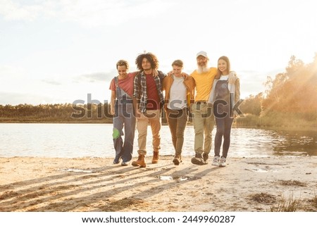 A bonded group of five strolls by the water's edge as the sun sets, casting a soft glow on their casual outing. Close-knit Friends Walking Together Along a Lakeshore at Dusk. High quality photo Royalty-Free Stock Photo #2449960287