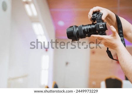 The person is holding a digital camera with their fingers on the camera lens and thumb on a camera accessory. The reflex camera is resting on their thigh, colored in magenta Royalty-Free Stock Photo #2449973229