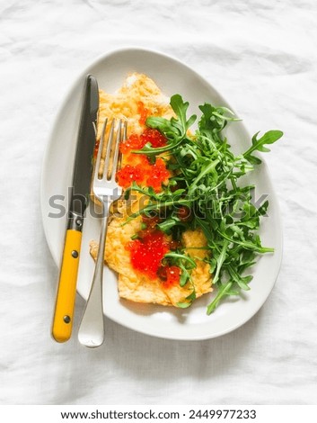 Cheese omelet with red caviar and arugula on a light background, top view