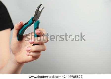 Woman with bent nose pliers on grey background, closeup. Space for text Royalty-Free Stock Photo #2449985579
