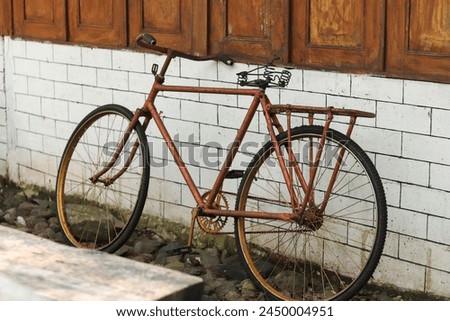 Indonesia - April 16, 2024 : Capture the charm of yesteryears with this vintage red bicycle leaning against weathered walls. A timeless symbol of nostalgia and uniqueness. 🚲 #VintageRed #BicycleCharm