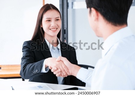 A young businesswoman smiles while shaking hands, making a positive impression during a professional meeting. Royalty-Free Stock Photo #2450006907