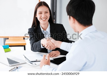 A young businesswoman smiles while shaking hands, making a positive impression during a professional meeting. Royalty-Free Stock Photo #2450006929