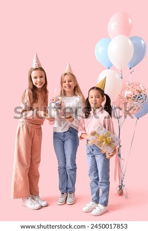 Cute little girls in party hats with Birthday cake and gift on pink background