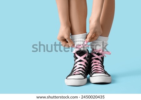 Young woman in sneakers with pink bows on blue background, closeup