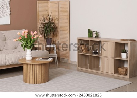 Interior of living room with chest of drawers, coffee table and vase with tulips