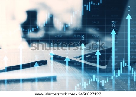 Close up of laptop and supplies at desk with growing blue vertical arrows and candlestick forex chart on blurry index grid background. Economic growth and increase concept. Double exposure
