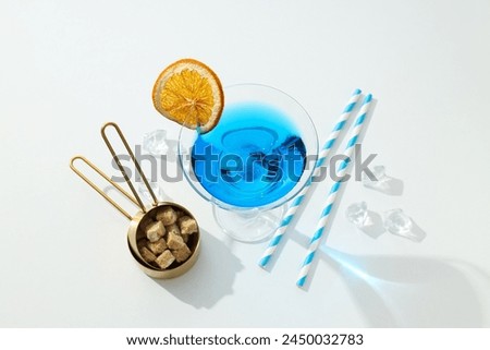 Blue cocktail in glass, orange slice, sugar and ice cubes on white background, top view