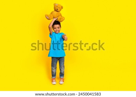 Full length photo of multiethnic multinational child dressed blue t-shirt jeans hold teddy bear over head isolated on yellow background Royalty-Free Stock Photo #2450041583