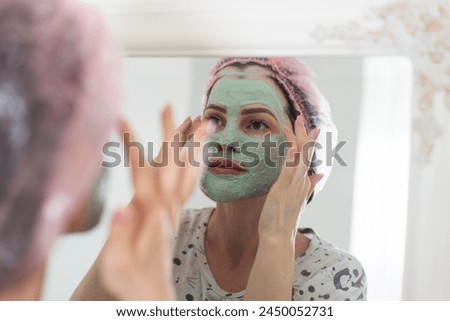  woman use a facial mask. She is looking in the mirror.