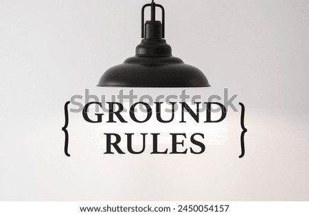 A sleek black pendant lamp illuminates the words Ground Rules on a clean background Royalty-Free Stock Photo #2450054157