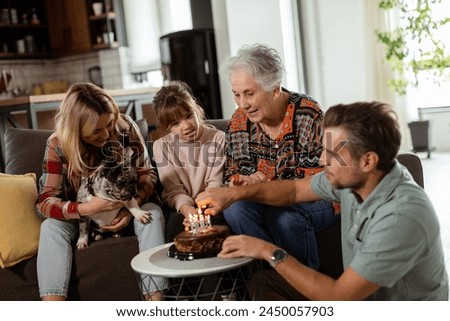 Heartwarming scene unfolds as a multi-generational family gathers on a couch to present a birthday cake to a delighted grandmother, creating memories to cherish Royalty-Free Stock Photo #2450057903